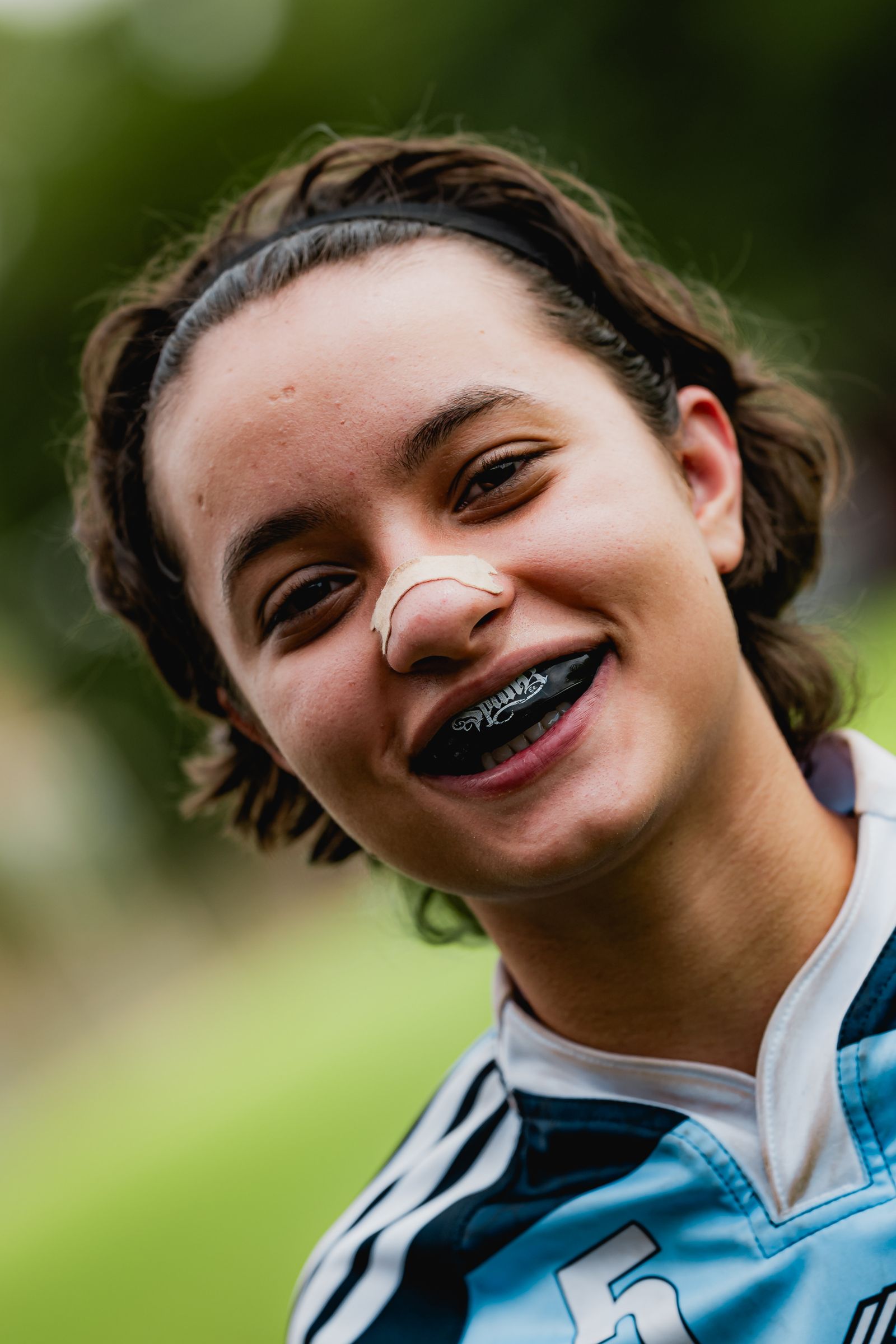 Teen athlete in a jersey smiling while wearing a black sports mouthguard