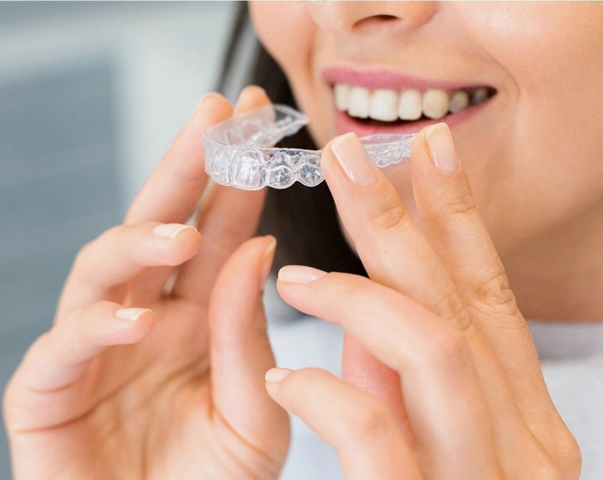Woman holding a clear Invisalign aligner tray up to her smile