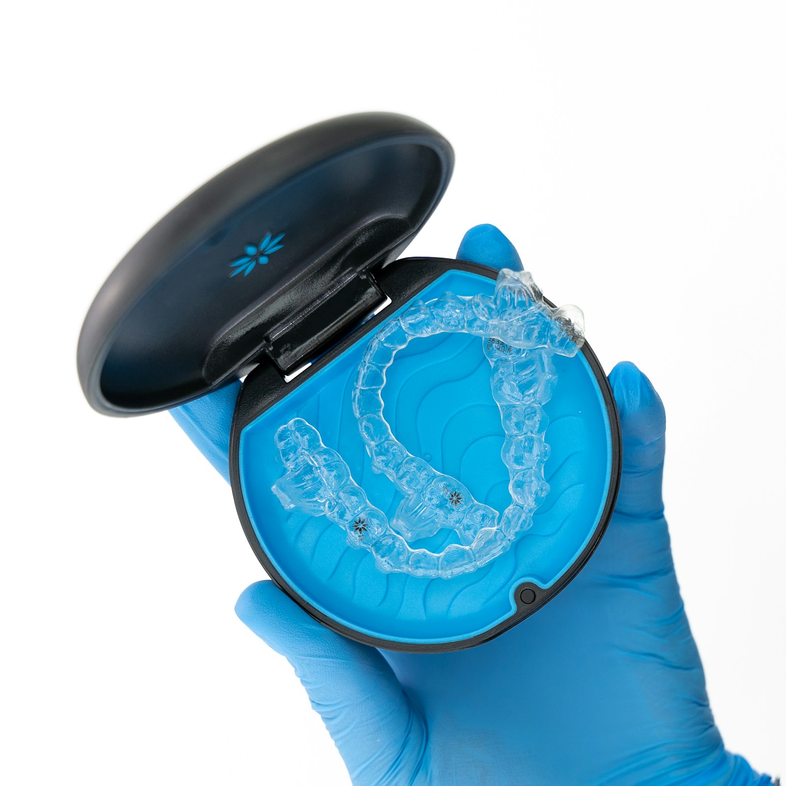 Gloved hand holding an open case with a clear Invisalign aligner inside