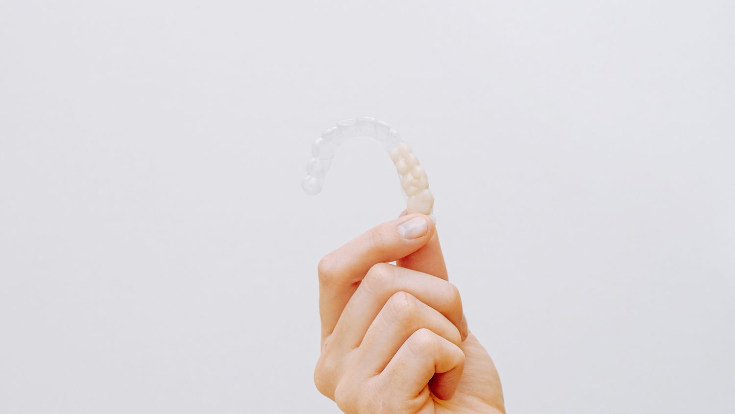 Hand holding a clear dental aligner, illustrating the importance of consistent Invisalign wear